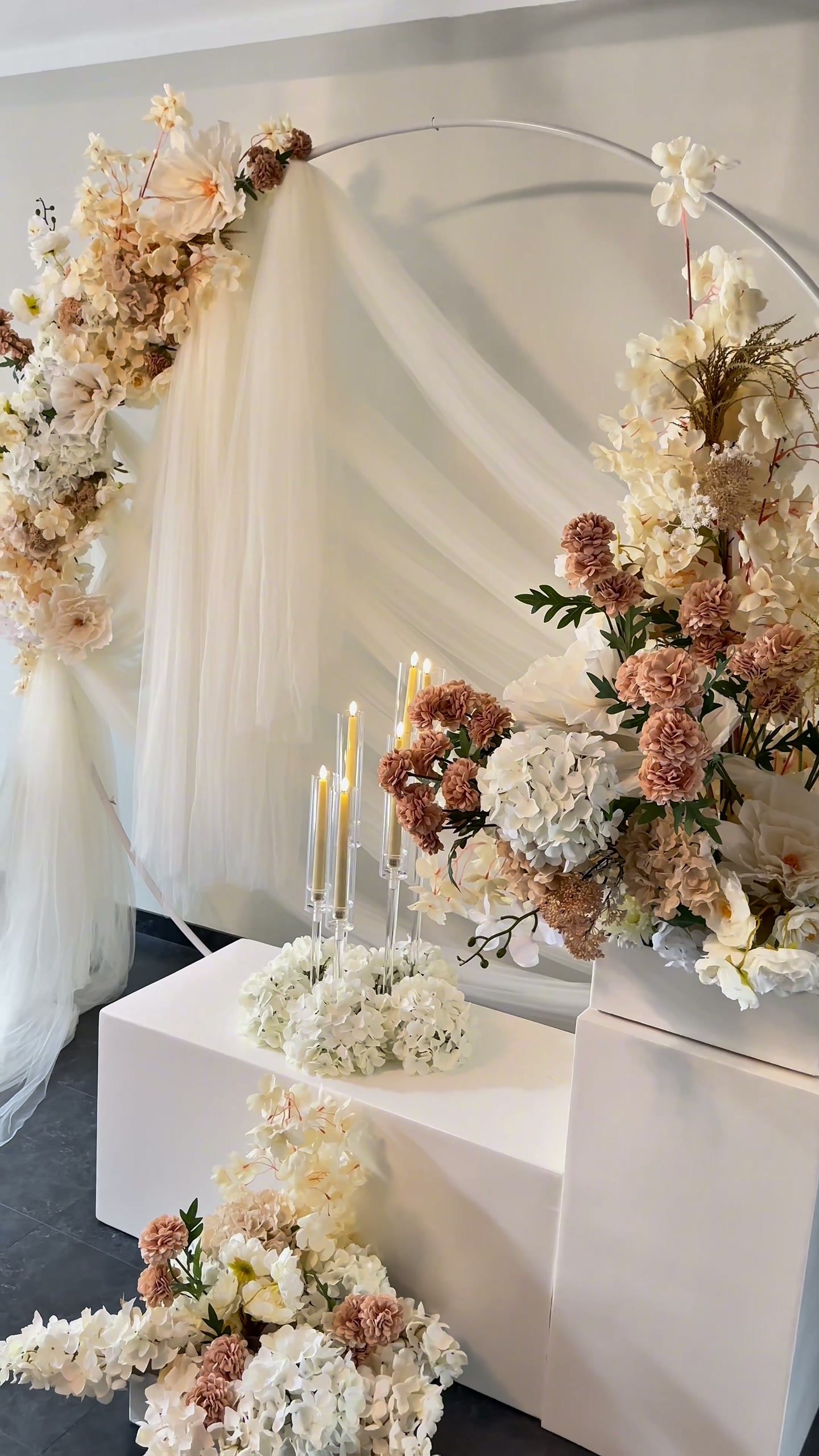 Witte voile-achterwand met bloemenboog en witte sokkels